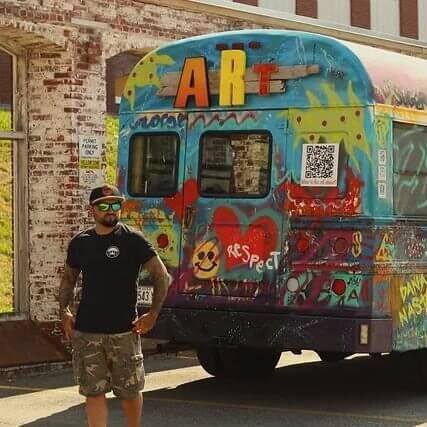 Man standing in front of an artfully painted school bus.